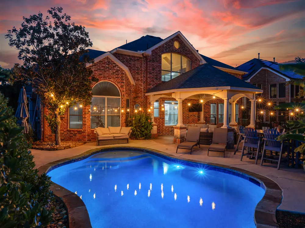 Twilight backyard with lit pool and covered patio